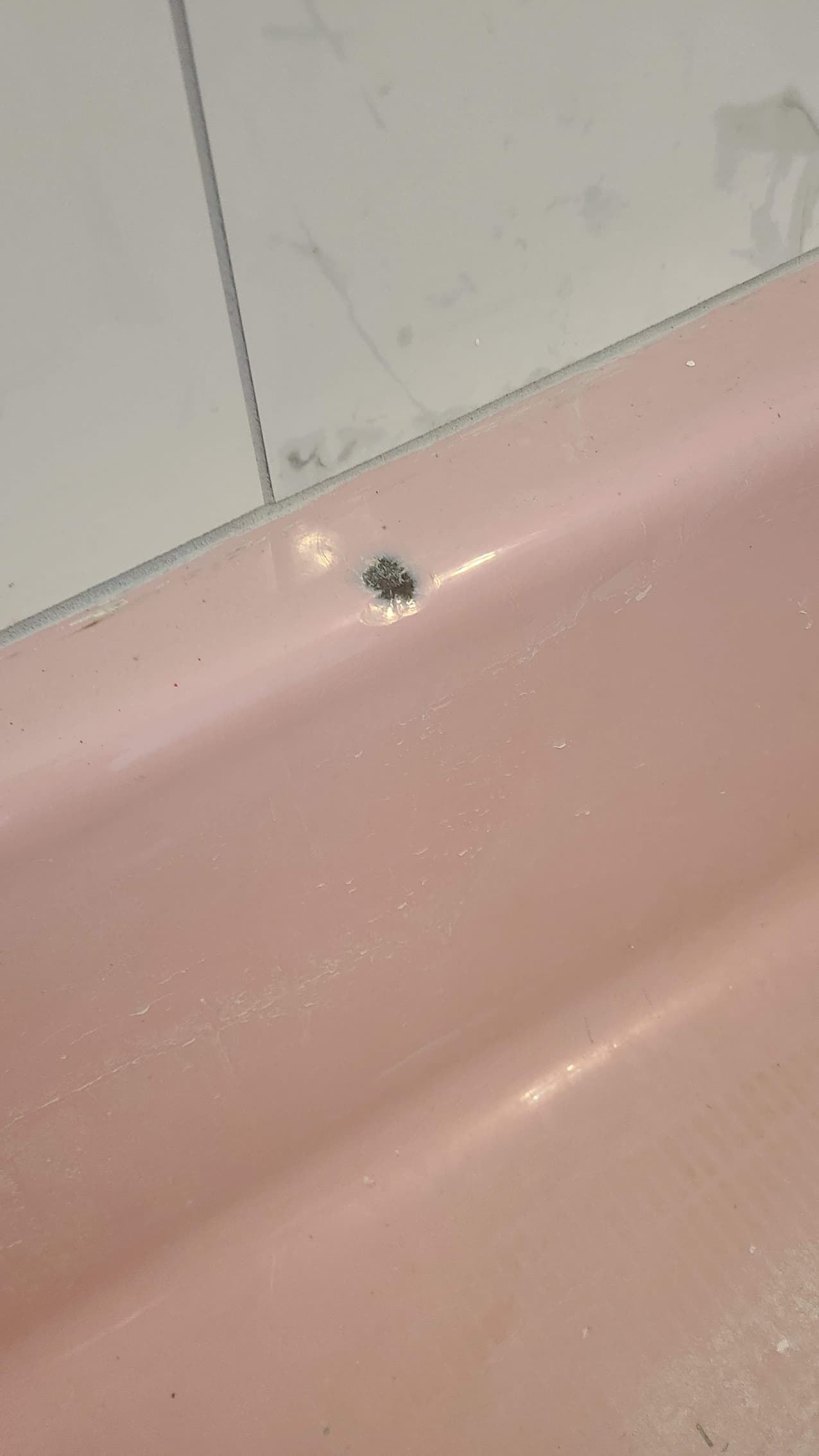 Small dark chip on the rim of a pink bathtub against white wall tiles.